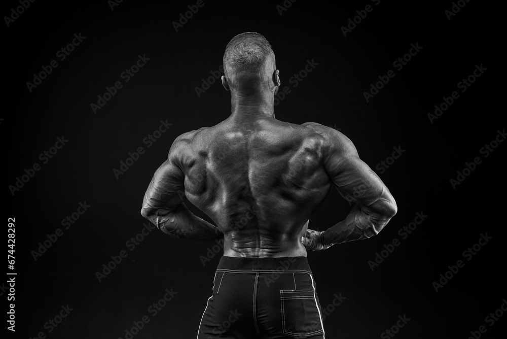 Fototapeta premium Silhouette of a strong bodybuilder. View from the back. Confident young fitness athlete with a powerful body and perfect abs. Black and white photography.