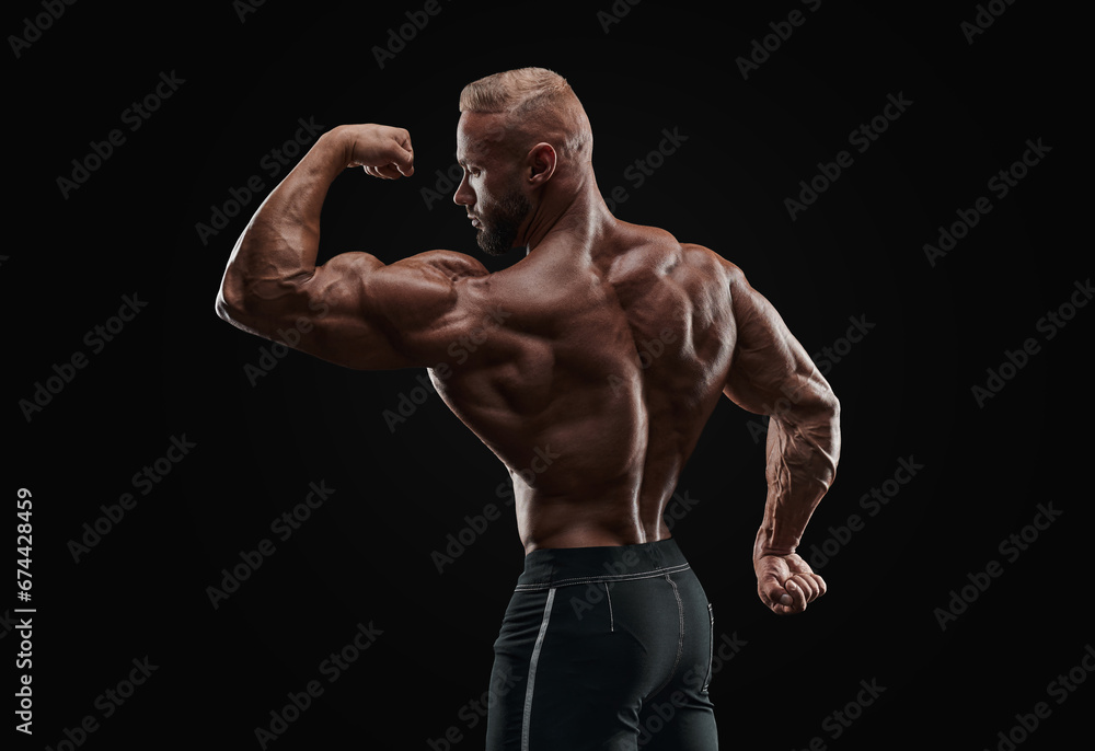 Muscular man showing back muscles, isolated on black background. Strong male rear view