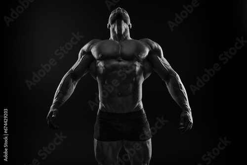 Silhouette of a strong bodybuilder. Confident young fitness athlete with a powerful body and perfect abs. Black and white photography. Dramatic light. © andy_gin