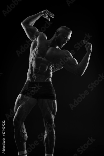 Silhouette of a strong bodybuilder. Confident young fitness athlete with a powerful body and perfect abs. Black and white photography. Dramatic light.