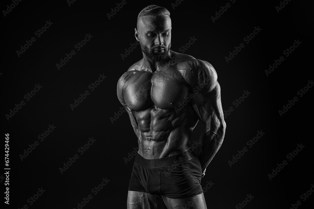Silhouette of a strong bodybuilder. Confident young fitness athlete with a powerful body and perfect abs. Black and white photography. Dramatic light.