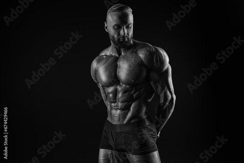 Silhouette of a strong bodybuilder. Confident young fitness athlete with a powerful body and perfect abs. Black and white photography. Dramatic light. © andy_gin