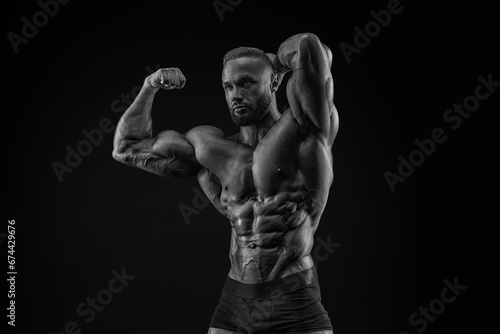 Silhouette of a strong bodybuilder. Confident young fitness athlete with a powerful body and perfect abs. Black and white photography. Dramatic light.