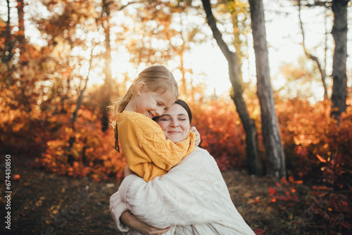 Young mother and her daughter walking together in a beautiful autumn forest.