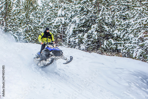 Snowmobile moving in the winter forest in the mountains. Man and fast action snowmobile jumping. Jumping on a snowmobile on a background of winter forest. Bright snowmobile