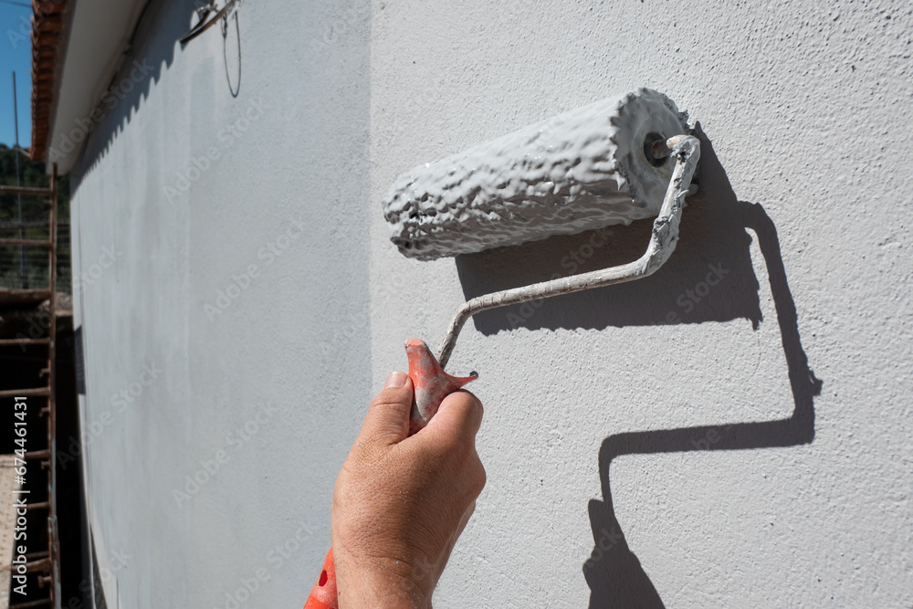Mão de pintor a segurar um rolo cheio de tinta para pintar uma parede exterior - obrazy, fototapety, plakaty 