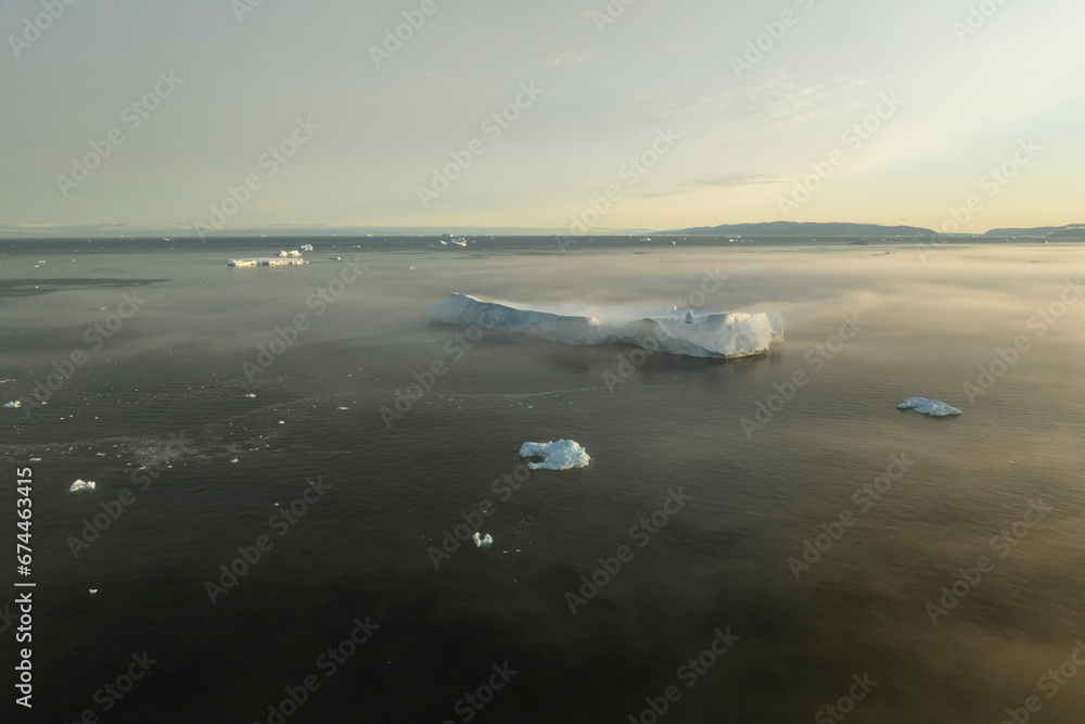 Aerial drone view a huge iceberg covered in fog at soft morning light in Ilulissat, Greenland, Arctic. Aerial drone view a huge iceberg covered in fog at soft morning light in Ilulissat, Greenland, Arctic.