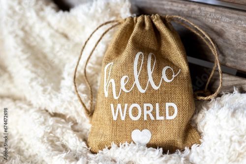 Brown jute drawstring pouch with heat-pressed white vinyl saying "Hello World" on soft white blanket.