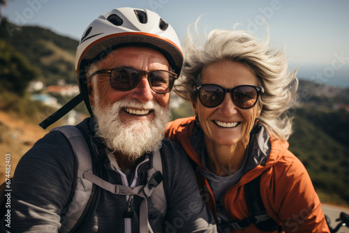 Close-up portrait of elderly smiling Caucasian couple riding bicycles together along picturesque country road. Cheerful seniors on a bike ride. Retired people lead active lifestyle to stay healthy.