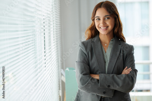 Portrait of smiling successful female entrepreneur in grey blazer standing at office window