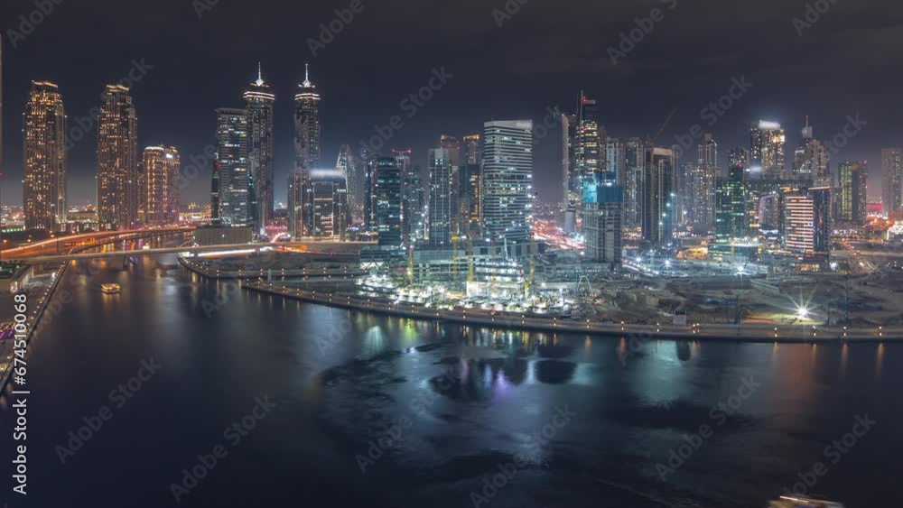 Cityscape panorama with illuminated skyscrapers of Dubai Business Bay and water canal aerial night timelapse. Modern skyline with residential and office towers on waterfront. Reflections in a river Cityscape panorama with illuminated skyscrapers of Dubai Business Bay and water canal aerial night timelapse. Modern skyline with residential and office towers on waterfront. Reflections in a river
