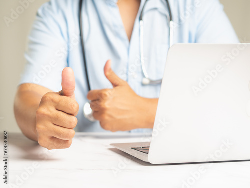 Doctor showing thumbs up to the success and best service while sitting at the table in the hospital.