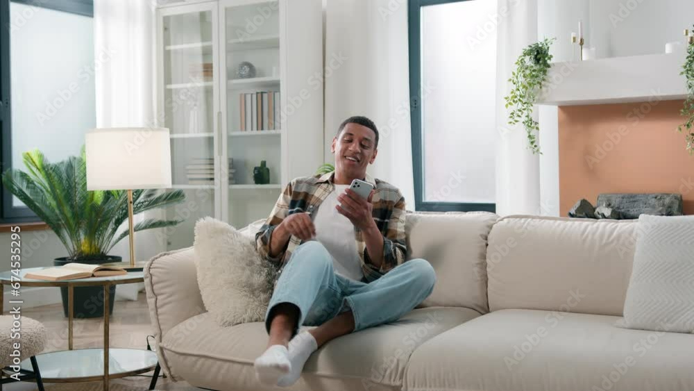 African American guy ethnic man male at home walk come in living room sit on couch looking mobile phone app using smartphone chatting reading social media relax resting on sofa relaxing browsing net African American guy ethnic man male at home walk come in living room sit on couch looking mobile phone app using smartphone chatting reading social media relax resting on sofa relaxing browsing net