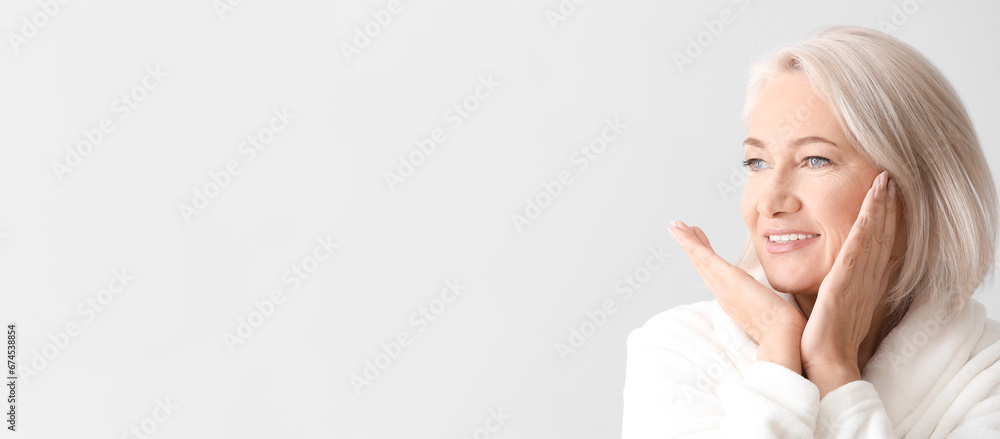 Mature woman giving herself face massage on light background with space for text Mature woman giving herself face massage on light background with space for text
