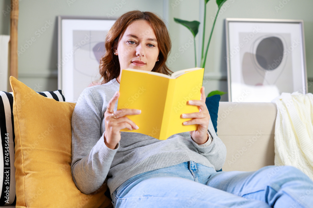 Young woman sitting on sofa and reading book Young woman sitting on sofa and reading book