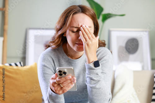 Cuadro en lienzo Frustrated young woman with a smartphone in hands while she sitting on the couch