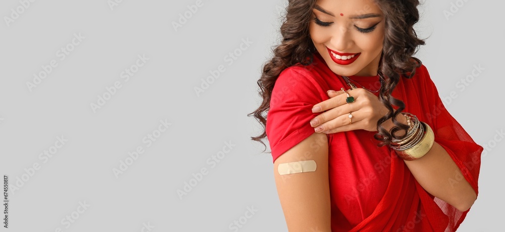 Beautiful Indian woman with medical patch on her arm against grey background with space for text. Vaccination concept Beautiful Indian woman with medical patch on her arm against grey background with space for text. Vaccination concept