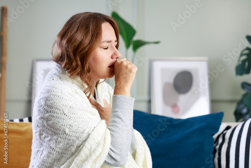 Sick woman sitting on couch and coughing while suffering from sore throat photo