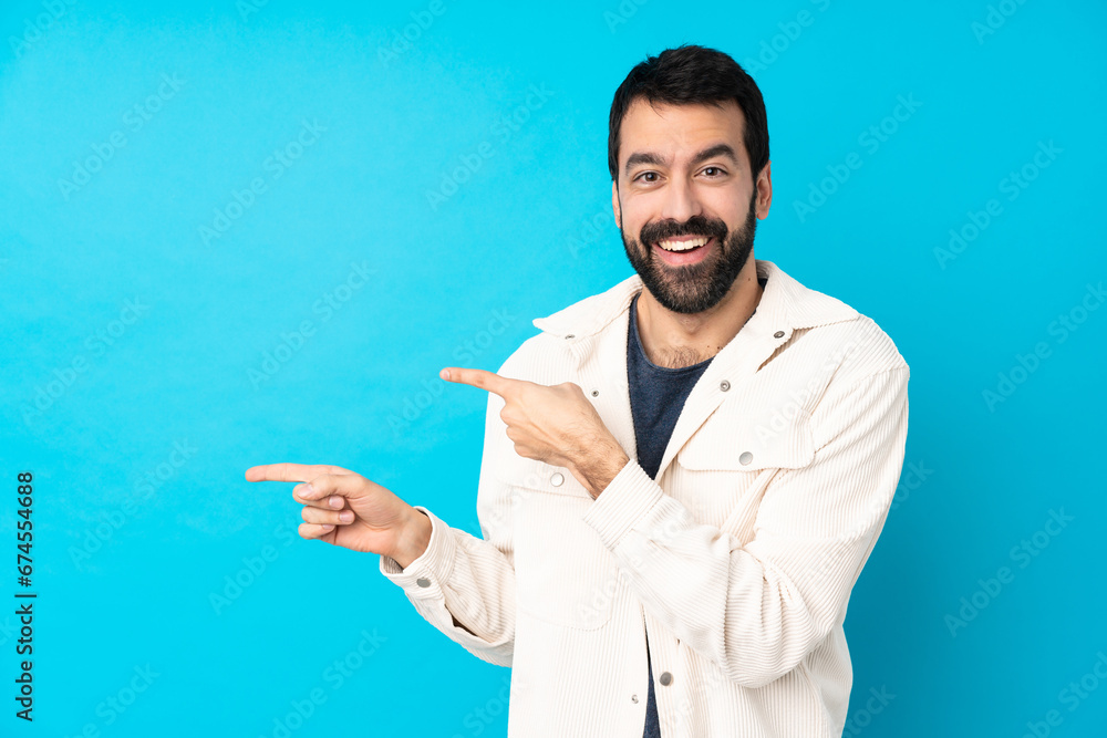 Young handsome man with white corduroy jacket over isolated blue background surprised and pointing side Young handsome man with white corduroy jacket over isolated blue background surprised and pointing side