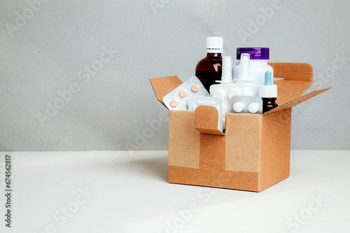 A set of medicines for treatment in bottles and tablets in transparent plates in a square cardboard box on a light background. Delivery of medicines. Front view