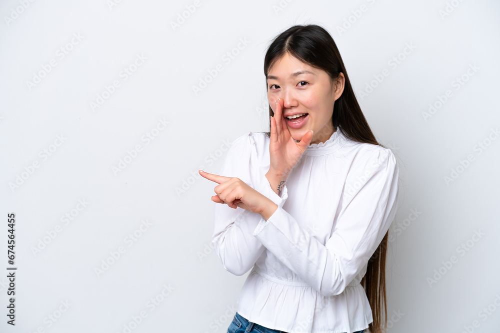 Young Chinese woman isolated on white background pointing to the side to present a product and whispering something