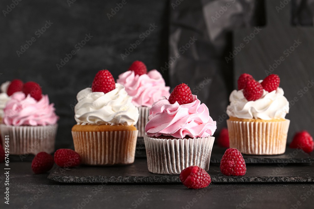 Boards of tasty raspberry cupcakes on black background