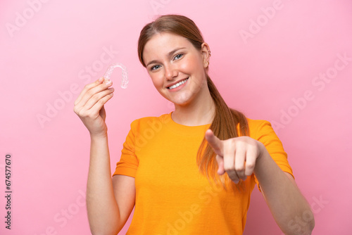 Young caucasian woman holding invisaging isolated on pink background points finger at you with a confident expression