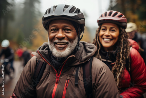 Happy smiling elderly couple in safety helmets riding bicycles together to stay fit and healthy. African American seniors having fun on a bike ride in autumn park. Active lifestyle for retired people.