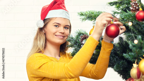 Happy young woman in cozy sweater decorating christmas tree with bauble at home