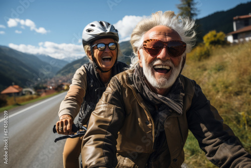 Elderly smiling Caucasian couple riding bicycles together along picturesque country road. Happy cheerful seniors on a bike ride. Retired people lead active lifestyle to stay fit and healthy.