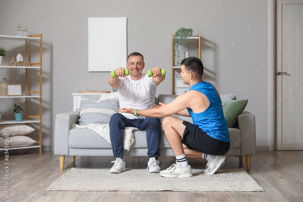 Mature man training with dumbbells and rehabilitation therapist at home