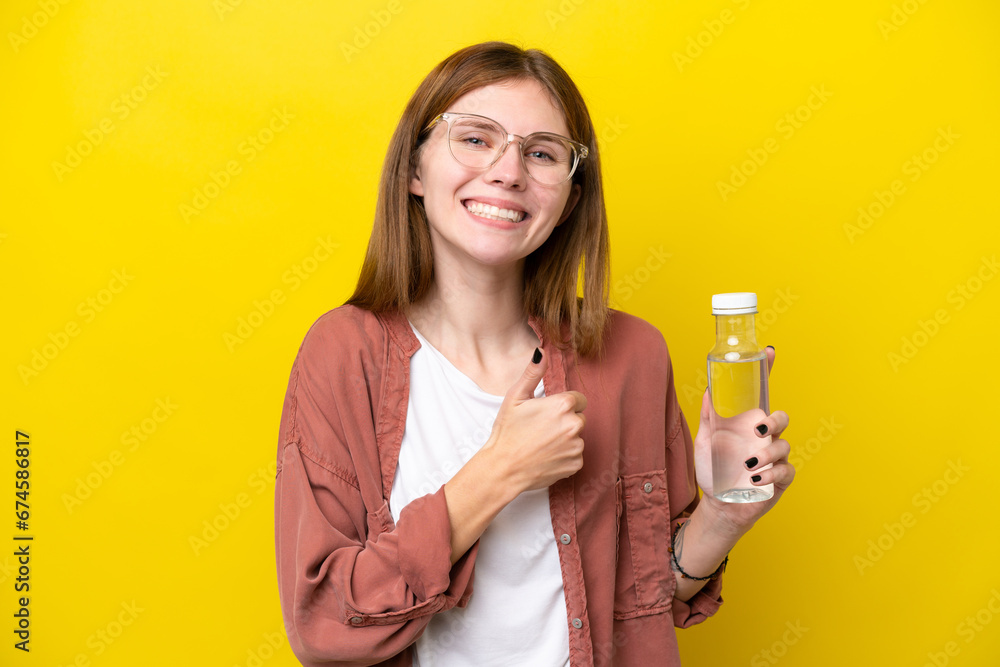 Young English woman with a bottle of water isolated on yellow background giving a thumbs up gesture Young English woman with a bottle of water isolated on yellow background giving a thumbs up gesture