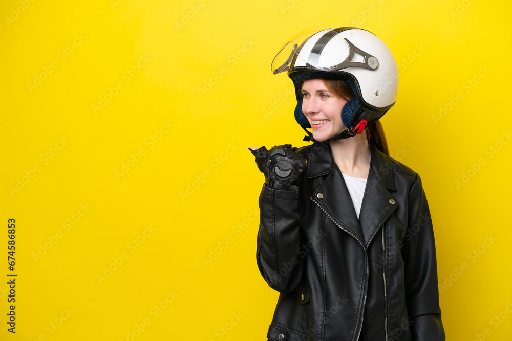 Young English woman with a motorcycle helmet isolated on yellow background pointing to the side to present a product Young English woman with a motorcycle helmet isolated on yellow background pointing to the side to present a product