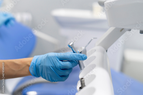 dentist in blue gloves taking drill of a dental machine instrument panel to treat patient in a clinic