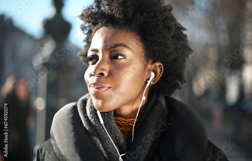portrait of smiling young black woman in the street listens to music