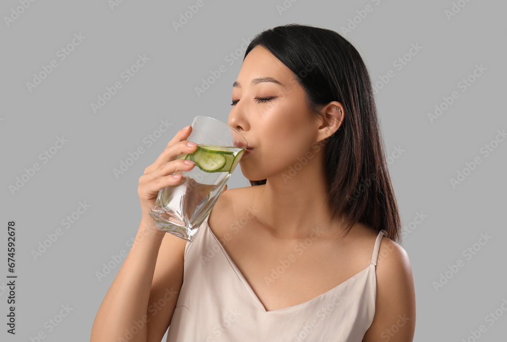 Beautiful Asian woman drinking cucumber water on grey background, closeup Beautiful Asian woman drinking cucumber water on grey background, closeup