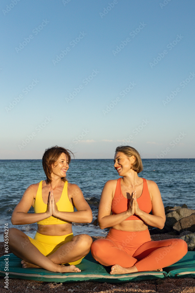 Two young beautiful girls sitting in meditation position on the beach at sunset Two young beautiful girls sitting in meditation position on the beach at sunset