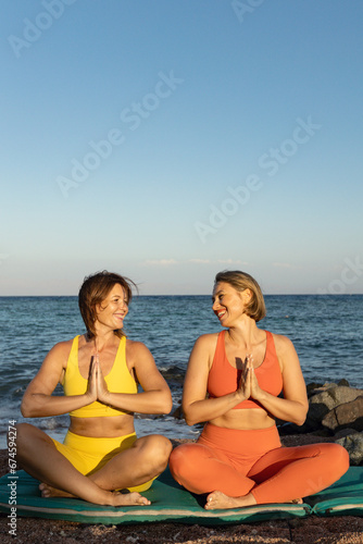 Two young beautiful girls sitting in meditation position on the beach at sunset