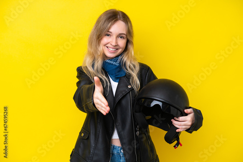 Blonde English young girl with a motorcycle helmet isolated on yellow background shaking hands for closing a good deal