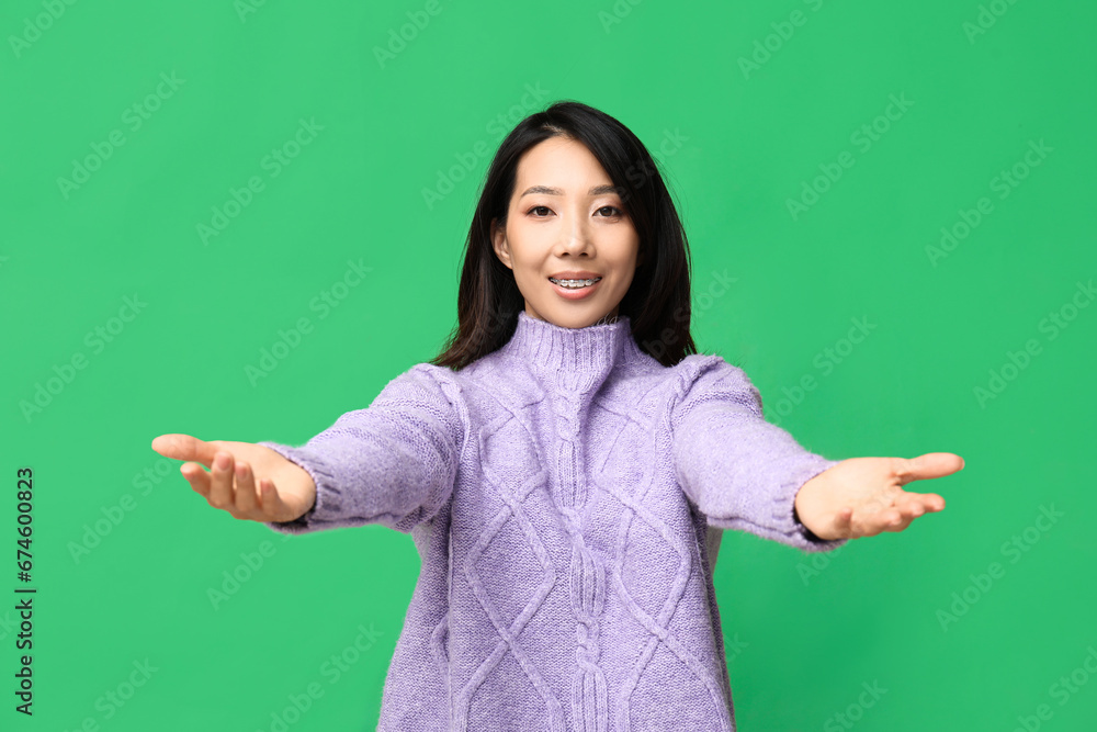 Young Asian woman opening arms for hug on green background Young Asian woman opening arms for hug on green background