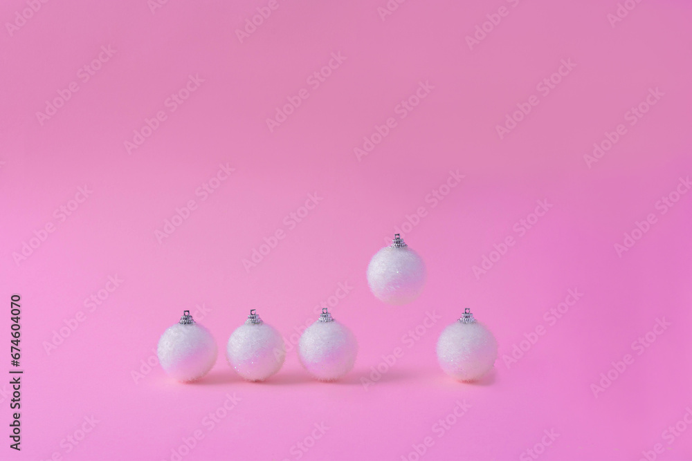 Creative layout made with a white Christmas bauble and a flying one on a pink pastel background. Minimal holiday decoration.