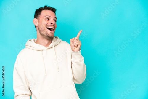 Young caucasian handsome man isolated on blue background intending to realizes the solution while lifting a finger up