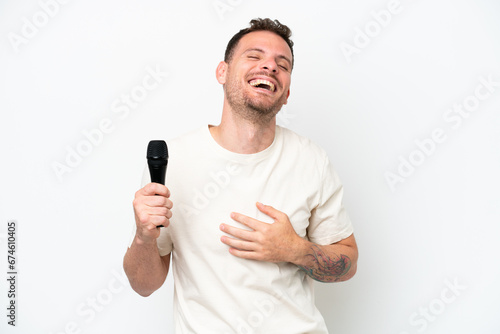 Young caucasian singer man picking up a microphone isolated on white background smiling a lot