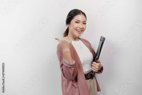 Excited Asian woman employee wearing cardigan pointing at the copy space beside her while holding s clipboard, isolated by white background photo