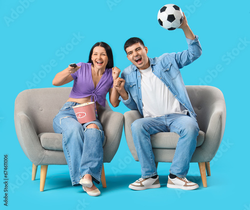 Cheerful young couple watching soccer match on TV against blue background photo