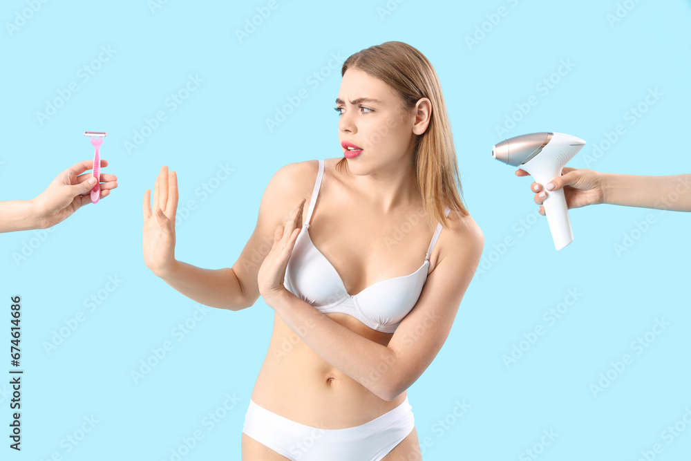 Displeased young woman and hands with supplies for hair removing on blue background Displeased young woman and hands with supplies for hair removing on blue background