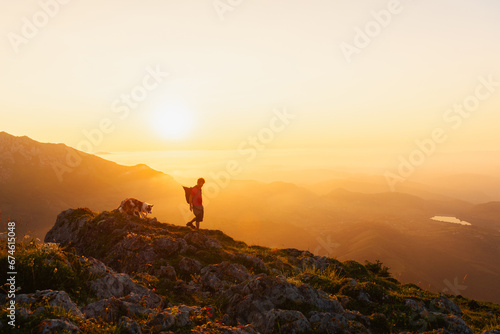 young man with backpack hiking with his border collie dog in the high mountains at sunset. sport, adventure and outdoor leisure.