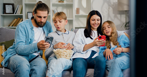 Happy family of four enjoy using smartphone technology relax sit in line on sofa holding smartphone ignoring friends chatting online in messenger mobile phone.