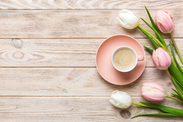 Spring background with flowers, a cup of coffee and a bouquet of pink and white tulips on colored table background with place for text. Copy space top view