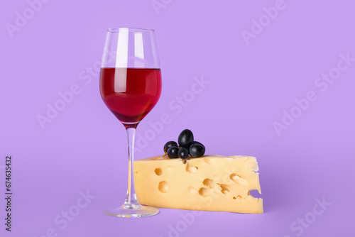 Glass of exquisite wine with cheese and grapes on lilac background
